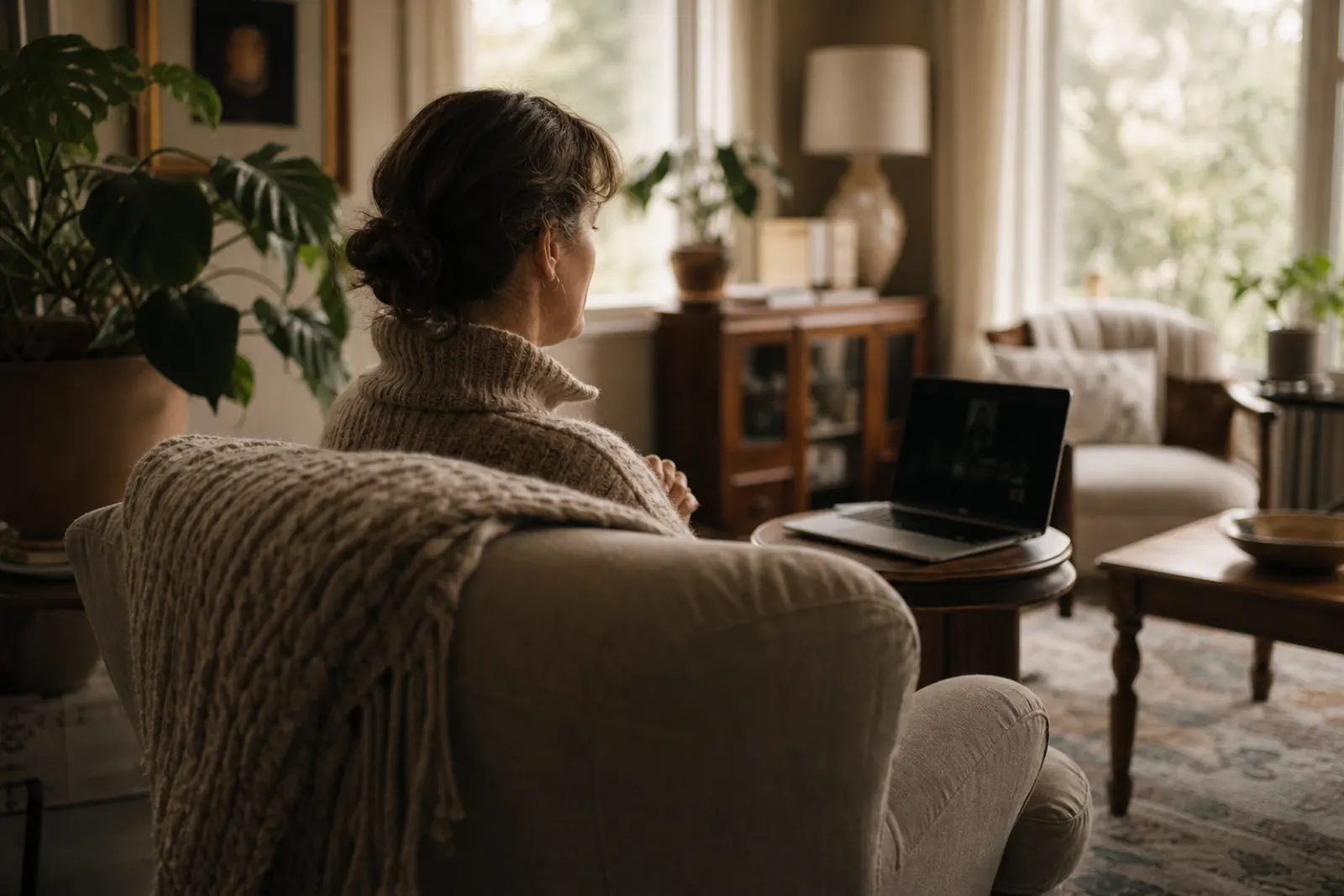 Woman in an armchair at home with a laptop on a side table, before a video call