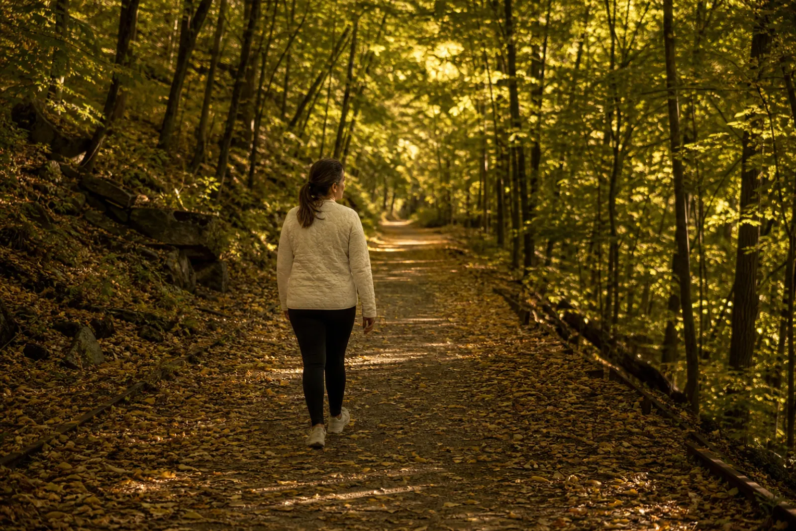 Woman walking a wooded rail trail under a green and gold canopy of trees